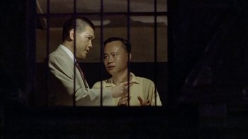Movie still from “The Quiet American” (2002), directed by Phillip Noyce – Two men in suits are standing in a jail cell; Medium shot, Over the shoulder angle