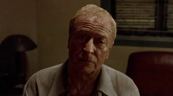 Movie still from “The Quiet American” (2002), directed by Phillip Noyce – An older man with a shaved head looks at the camera; Close Up shot, Over the shoulder angle