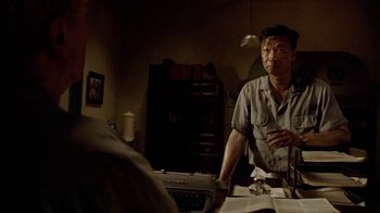 Movie still from “The Quiet American” (2002), directed by Phillip Noyce – A man standing next to a table in a living room; Medium shot, Over the shoulder angle