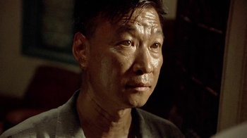 Movie still from “The Quiet American” (2002), directed by Phillip Noyce – An asian man with a shaved head looking at the camera; Close Up shot, Low angle
