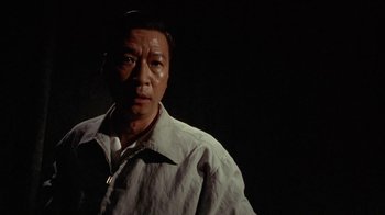 Movie still from “The Quiet American” (2002), directed by Phillip Noyce – A man in a white shirt is standing in a dark room; Close Up shot, Low angle