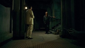 Movie still from “The Quiet American” (2002), directed by Phillip Noyce – Two men in suits are standing in a dark room; Wide shot, High angle