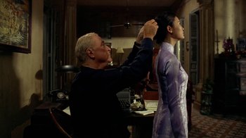 Movie still from “The Quiet American” (2002), directed by Phillip Noyce – An older man and a young woman are getting their hair done; Medium shot, Over the shoulder angle