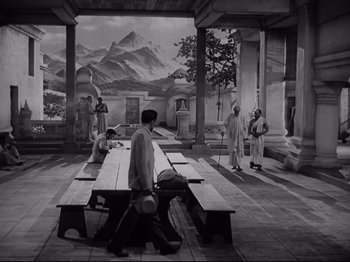 Movie still from “The Razor's Edge” (1946), directed by Edmund Goulding – A black - and - white photo of a man standing next to a bench; Extreme Wide shot, High angle