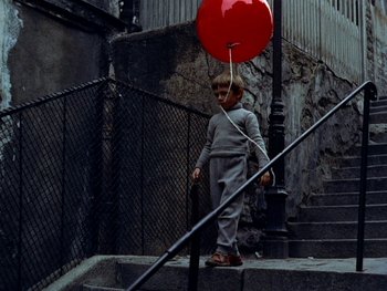 Movie still from “The Red Balloon” (1956), directed by Albert Lamorisse – A young boy holding onto a red balloon; Wide shot, Low angle