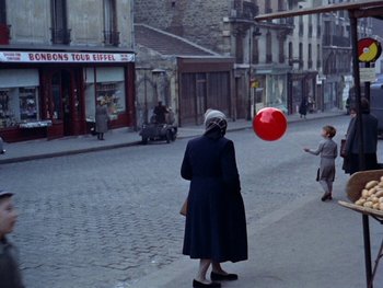 Movie still from “The Red Balloon” (1956), directed by Albert Lamorisse – An older woman is playing with a red balloon; Extreme Wide shot, High angle