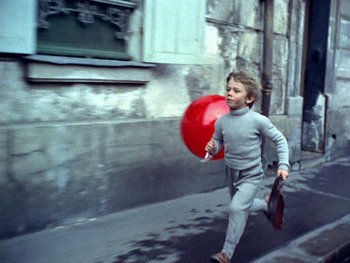 Movie still from “The Red Balloon” (1956), directed by Albert Lamorisse – A young boy running down the street with a red balloon; Wide shot, High angle