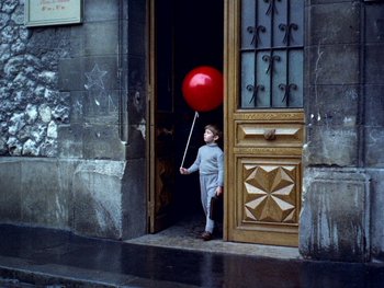 Movie still from “The Red Balloon” (1956), directed by Albert Lamorisse – A boy holding a red balloon in front of a door; Wide shot, High angle