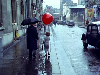 Movie still from “The Red Balloon” (1956), directed by Albert Lamorisse – A child and an adult walking down a street holding umbrellas; Extreme Wide shot, High angle