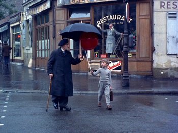 Movie still from “The Red Balloon” (1956), directed by Albert Lamorisse – A man and a child walking down the street holding an umbrella; Wide shot, High angle