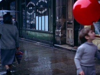 Movie still from “The Red Balloon” (1956), directed by Albert Lamorisse – Two people walking down a street with a red balloon; Wide shot, High angle