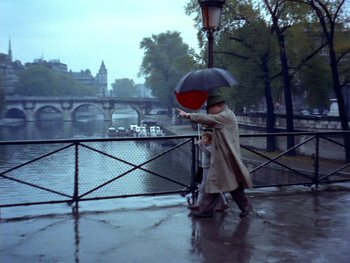 Movie still from “The Red Balloon” (1956), directed by Albert Lamorisse – A man holding an umbrella while standing on a bridge; Wide shot, High angle