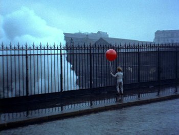 Movie still from “The Red Balloon” (1956), directed by Albert Lamorisse – A little girl holding a red balloon near a fence; Extreme Wide shot, High angle