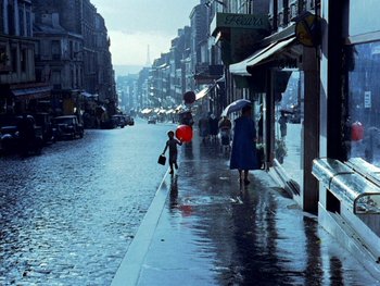 Movie still from “The Red Balloon” (1956), directed by Albert Lamorisse – A woman with an umbrella walking down a street; Extreme Wide shot, High angle