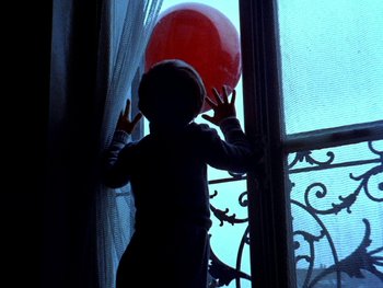 Movie still from “The Red Balloon” (1956), directed by Albert Lamorisse – A child standing in front of an open window with a red balloon; Wide shot, Low angle