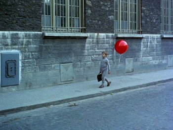 Movie still from “The Red Balloon” (1956), directed by Albert Lamorisse – A man walking down the street with a red balloon; Wide shot, High angle