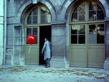 Movie still from “The Red Balloon” (1956), directed by Albert Lamorisse – A man holding a red balloon in front of a building; Extreme Wide shot, Low angle