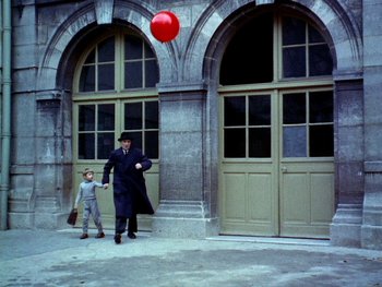 Movie still from “The Red Balloon” (1956), directed by Albert Lamorisse – A man and a boy walking in front of a building; Wide shot, Low angle