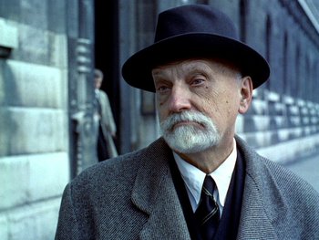 Movie still from “The Red Balloon” (1956), directed by Albert Lamorisse – An old man with a beard wearing a suit and a hat; Close Up shot, Low angle