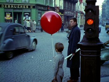 Movie still from “The Red Balloon” (1956), directed by Albert Lamorisse – A man and a boy are standing on the side of the street; Wide shot, Low angle