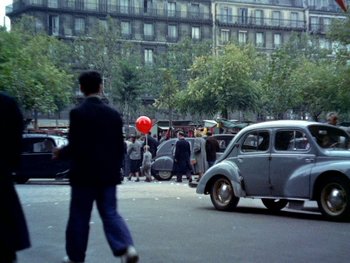 Movie still from “The Red Balloon” (1956), directed by Albert Lamorisse – A man walking down the street with a red balloon in his hand; Wide shot, High angle
