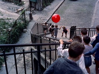 Movie still from “The Red Balloon” (1956), directed by Albert Lamorisse – A group of children playing with a red balloon; Extreme Wide shot, Overhead angle