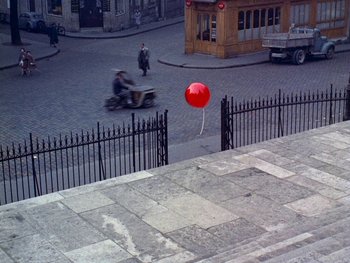 Movie still from “The Red Balloon” (1956), directed by Albert Lamorisse – A street scene with a person riding a scooter and a red balloon; Extreme Wide shot, Overhead angle