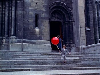 Movie still from “The Red Balloon” (1956), directed by Albert Lamorisse – A young boy holding a red balloon while walking down the steps; Extreme Wide shot, High angle