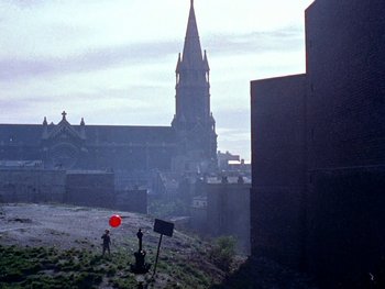 Movie still from “The Red Balloon” (1956), directed by Albert Lamorisse – A person holding a red balloon while standing on a hill near a church; Extreme Wide shot, High angle