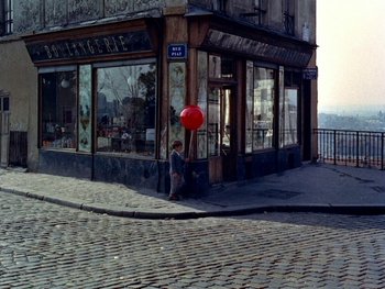 Movie still from “The Red Balloon” (1956), directed by Albert Lamorisse – A person holding a red balloon in front of a store; Extreme Wide shot, High angle