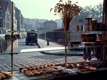 Movie still from “The Red Balloon” (1956), directed by Albert Lamorisse – A street view of a street with a bunch of pastries on the table; Wide shot, High angle