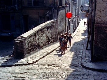 Movie still from “The Red Balloon” (1956), directed by Albert Lamorisse – A group of people walking down a brick street; Extreme Wide shot, High angle