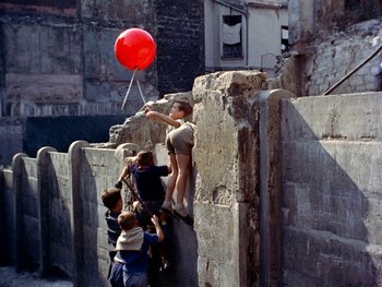 Movie still from “The Red Balloon” (1956), directed by Albert Lamorisse – A group of children standing next to each other holding a balloon; Wide shot, Overhead angle