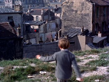 Movie still from “The Red Balloon” (1956), directed by Albert Lamorisse – A young boy standing on top of a grass covered hill; Wide shot, High angle