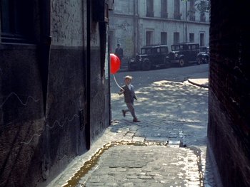 Movie still from “The Red Balloon” (1956), directed by Albert Lamorisse – A boy walking down the street holding a red balloon; Extreme Wide shot, High angle
