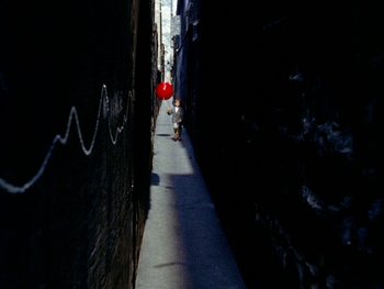 Movie still from “The Red Balloon” (1956), directed by Albert Lamorisse – A person walking down a street with a red balloon; Extreme Wide shot, Overhead angle