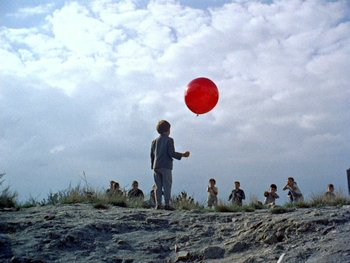 Movie still from “The Red Balloon” (1956), directed by Albert Lamorisse – A child is holding a balloon in the air; Wide shot, Low angle