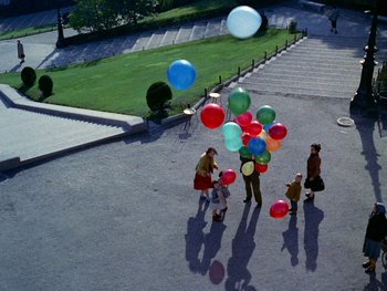 Movie still from “The Red Balloon” (1956), directed by Albert Lamorisse – A group of people standing on the side of a road holding balloons; Extreme Wide shot, Overhead angle