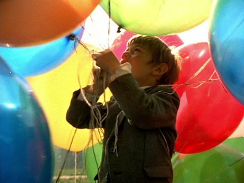Movie still from “The Red Balloon” (1956), directed by Albert Lamorisse – A little boy that is standing in a bunch of balloons; Medium shot, Low angle