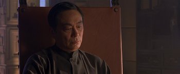 Movie still from “The Replacement Killers” (1998), directed by Antoine Fuqua – An older man sitting in front of an orange wall; Close Up shot, Over the shoulder angle