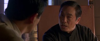 Movie still from “The Replacement Killers” (1998), directed by Antoine Fuqua – A man sitting in front of another man in front of a table; Close Up shot, Over the shoulder angle