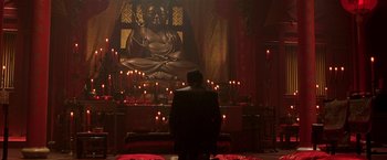 Movie still from “The Replacement Killers” (1998), directed by Antoine Fuqua – A man sitting in front of a large buddha statue; Wide shot, Low angle