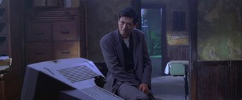 Movie still from “The Replacement Killers” (1998), directed by Antoine Fuqua – A man in a suit sitting in front of a table; Medium shot, Over the shoulder angle