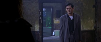 Movie still from “The Replacement Killers” (1998), directed by Antoine Fuqua – A man in a suit standing in front of an open door; Medium shot, Over the shoulder angle