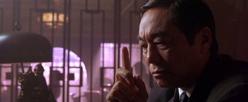 An older asian man is pointing his finger up