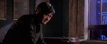 Movie still from “The Replacement Killers” (1998), directed by Antoine Fuqua – A man sitting in front of a table in a dark room; Close Up shot, Over the shoulder angle