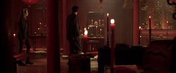Movie still from “The Replacement Killers” (1998), directed by Antoine Fuqua – A man standing in a dark room next to candles; Wide shot, High angle