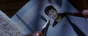 Movie still from “The Replacement Killers” (1998), directed by Antoine Fuqua – A person holding a pair of scissor in front of a picture of a man; Extreme Close Up shot, Overhead angle