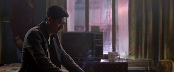 Movie still from “The Replacement Killers” (1998), directed by Antoine Fuqua – A man sitting in front of a tv in a room; Medium shot, Over the shoulder angle