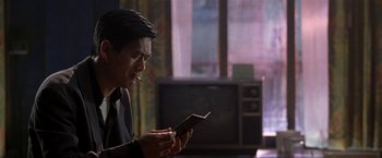 Movie still from “The Replacement Killers” (1998), directed by Antoine Fuqua – A man holding an electronic device in front of a television; Close Up shot, Over the shoulder angle